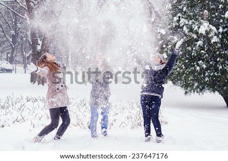Three teenage girls throwing snow in the air on cold winter day.