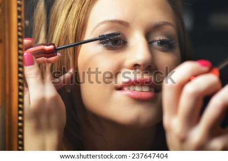 Beautiful young woman having fun while putting make up in front of the old mirror.