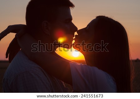 Silhouettes of young couple kissing at summer sunset.