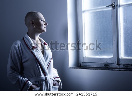 Bald woman suffering from cancer looking through the hospital window.