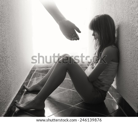 Depressed teenager sitting on the floor while hand coming out from bright background offers support in sepia tones.