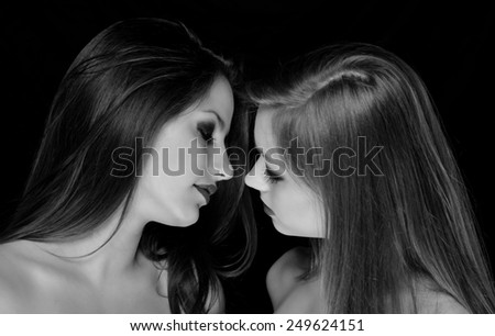 Profiles of two beautiful girls being intimate isolated on black background. Black and white photo.