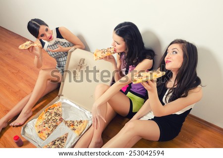 Cross processed image of three beautiful young ladies eating pizza while sitting on the floor.