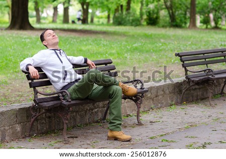 Young man sitting on the bench in the park and enjoying beautiful spring day.