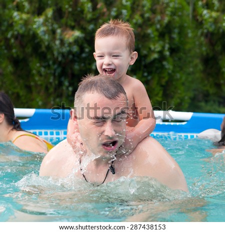 Father and son having fun in the swimming pool on hot summer day.