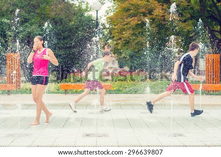 Teenage boys and girls having fun in the towns water fountain on hot summer day.