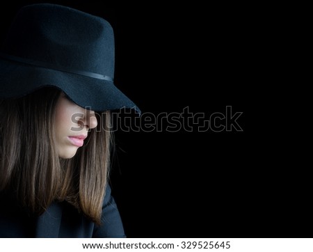 Beautiful elegant woman in black suit and black hat isolated on black background.