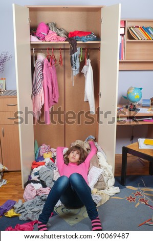Untidy teenage girl lying on pile of wrinkled clothes inside her wardrobe and daydreaming