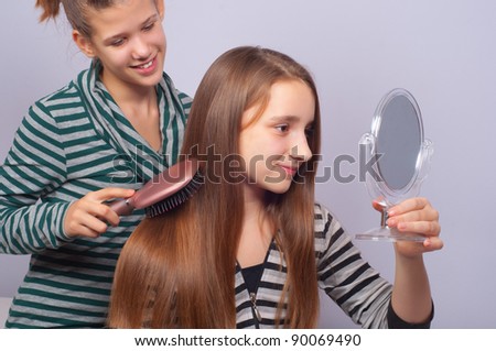 Pretty teenage girls combing hair and watching themselves in mirror