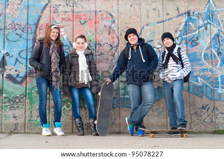 Happy teenage friends with school bags and skateboards standing in front of the graffiti wall.