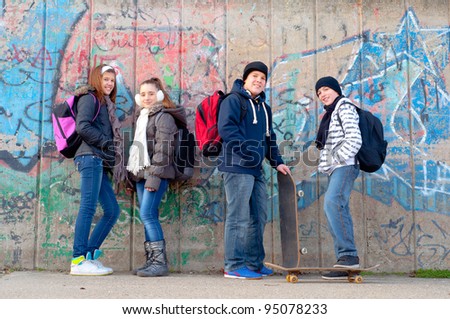 Happy teenage friends with school bags and skateboards standing in front of the graffiti wall.