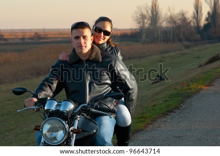 Young happy couple riding a motorcycle at sunset on beautiful autumn day.
