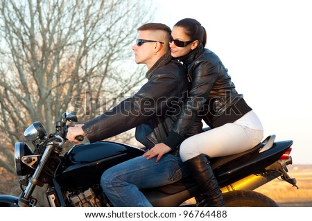 Young happy couple ready to go on a ride with motorcycle on beautiful autumn day.