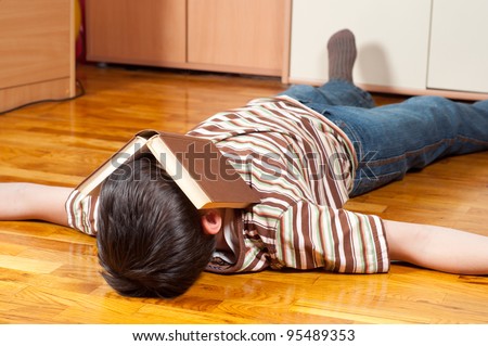 Teenage boy sleeping on the floor with book covering his face.