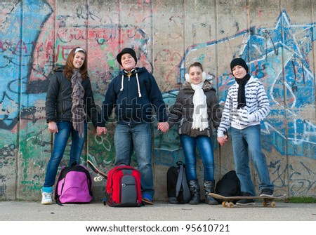 Teenage boys and girls with school bags and skateboard holding hands outdoor on beautiful autumn day.