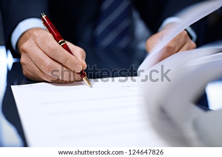 Businessman sitting at shiny office desk signing a contract with noble pen