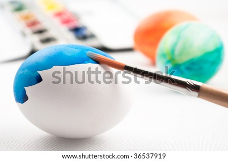 Half painted easter egg with complete painted eggs and watercolor palette in background.