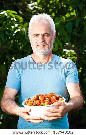 smiling senior man holding dish with strawberry