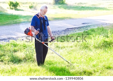worker cutting grass in garden with the weed trimmer