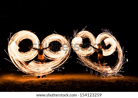 two fire dancers quickly spinning poi-snake with fire, creating giant circles of fire in the air