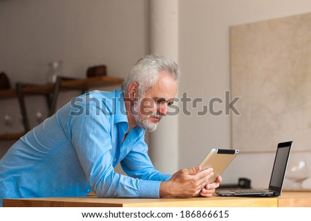 old man with notebook  at the kitchen and tablet in hands