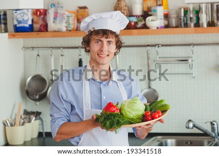 Friendly chef with a plate of vegetables smiling in his kitchen