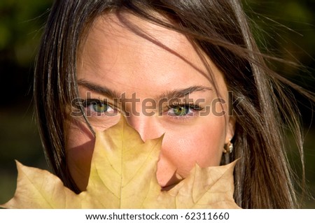 Beautiful young woman holding a maple leaf. Looks into the camera with green eyes. Autumn portrait.