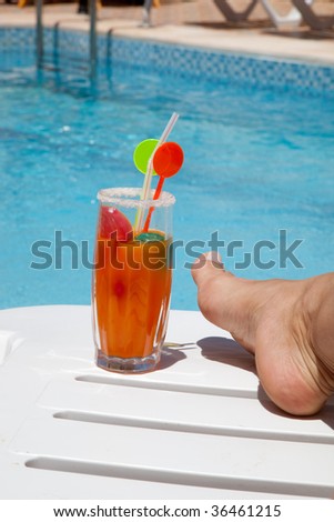Female foot and drink on a deck chair next to the pool