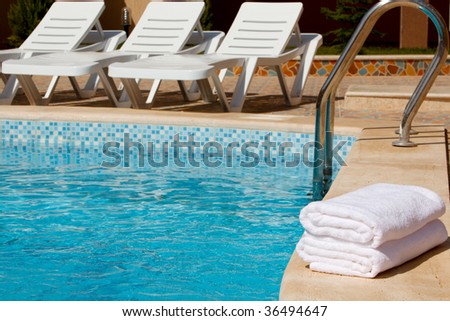 White towels by the pool with deck chairs in the back