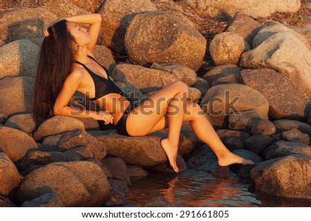 Woman in black bikini sitting on stones