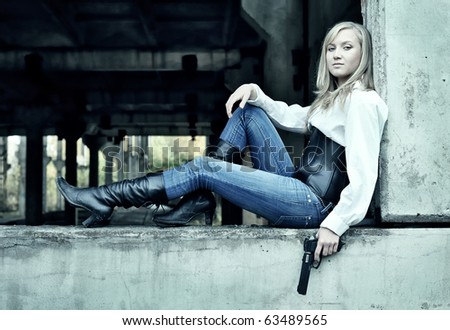 Woman with pistol in her hands sitting on the wall