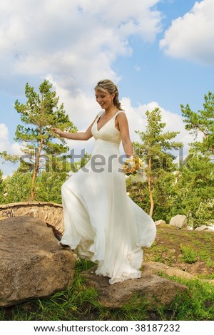The bride goes on stones. The joyful bride. Summer, day, nature, the blue sky with clouds