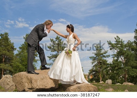 The groom kisses a hand of the bride. Clear sunny day, the blue sky and white clouds.