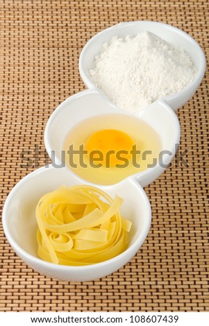 Pasta, egg yolk and flour on straw background