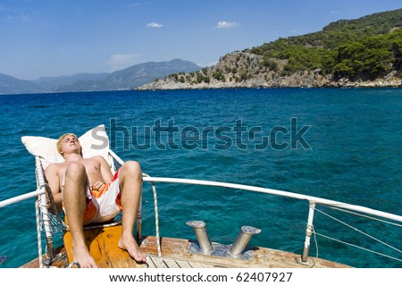 Young man relaxing, sunbathing on a boat during his summer holiday.