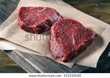 Succulent tender raw lean beef steaks lying on a sheet of oven paper in the kitchen topped ready to be cooked for dinner