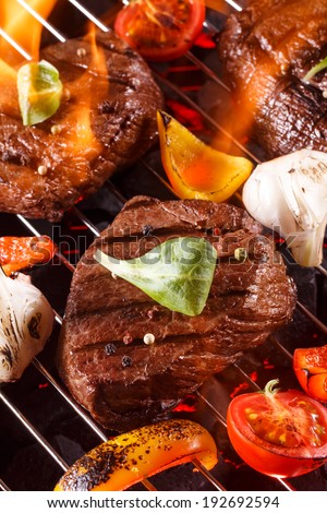 Beef steak on a barbecue grill with flames with vegetables