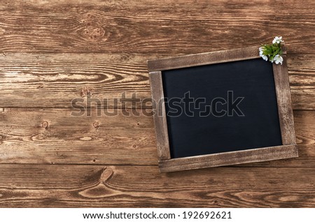 Old blank vintage school slate or chalkboard lying on an old rustic wooden background with dainty white flowers in two corners ready for your text or message