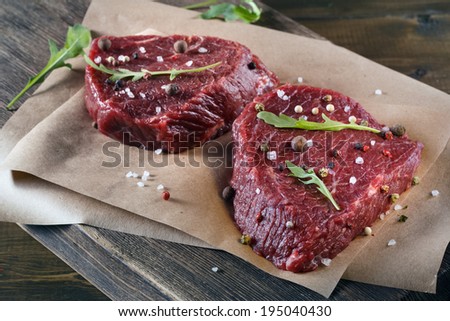 Succulent tender raw lean beef steaks lying on a sheet of oven paper in the kitchen topped with fresh herbs and spices ready to be cooked for dinner
