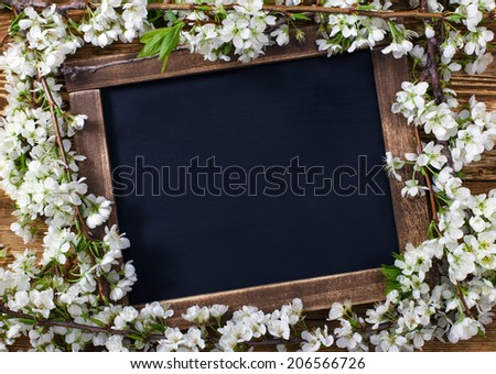 Old blank vintage school slate or chalkboard lying on an old rustic wooden background with dainty white flowers in two corners ready for your text or message