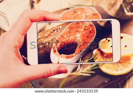 Using smartphones to take photos of raw salmon steak on wooden cutting board with instagram style filter.