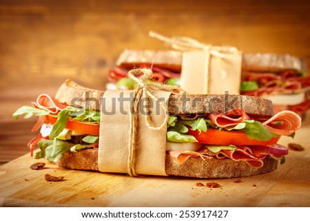 Two sandwiches with bacon and fresh vegetables on vintage wooden cutting board.Close-up.