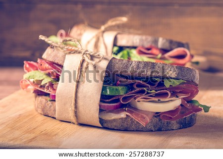 Two sandwiches with bacon and fresh vegetables on vintage wooden cutting board.  In the style of instagram filter. Close-up.