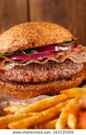 Burger and french fries with meat and vegetables close up on a cutting board on wooden background