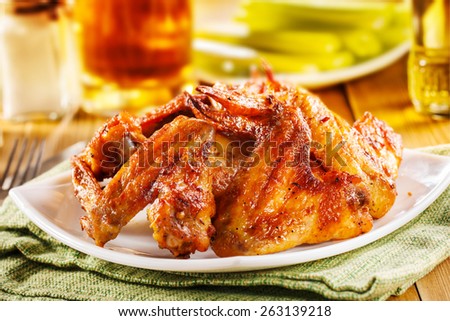 Roasted wings on the plate with sauce and beer on background, close-up.