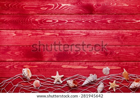 Sea and marine items such as seashells on red wooden background.