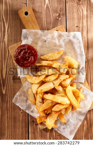 Fried Potatoes on old wooden cutting board with bowl ketchup. Top view.