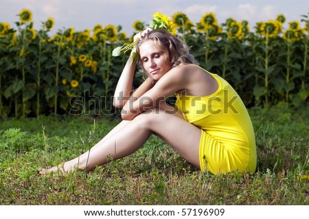 Beautiful girl in yellow clothes sits in the field with sunflowers