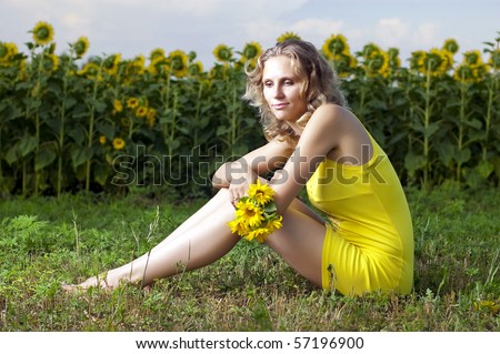 Beautiful girl in yellow clothes sits in the field with sunflowers