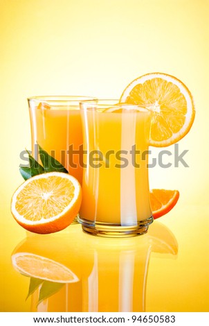 Two Glasses of Fresh Orange juice, half oranges and the leaves on yellow background